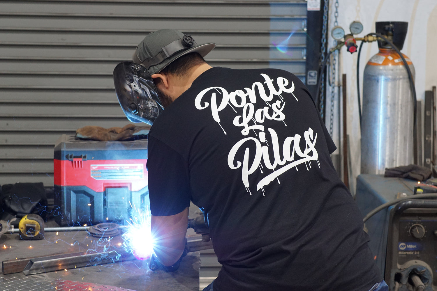 Latino welder wearing Ponte Las Pilas drip design t-shirt welding on job site - authentic workwear in action