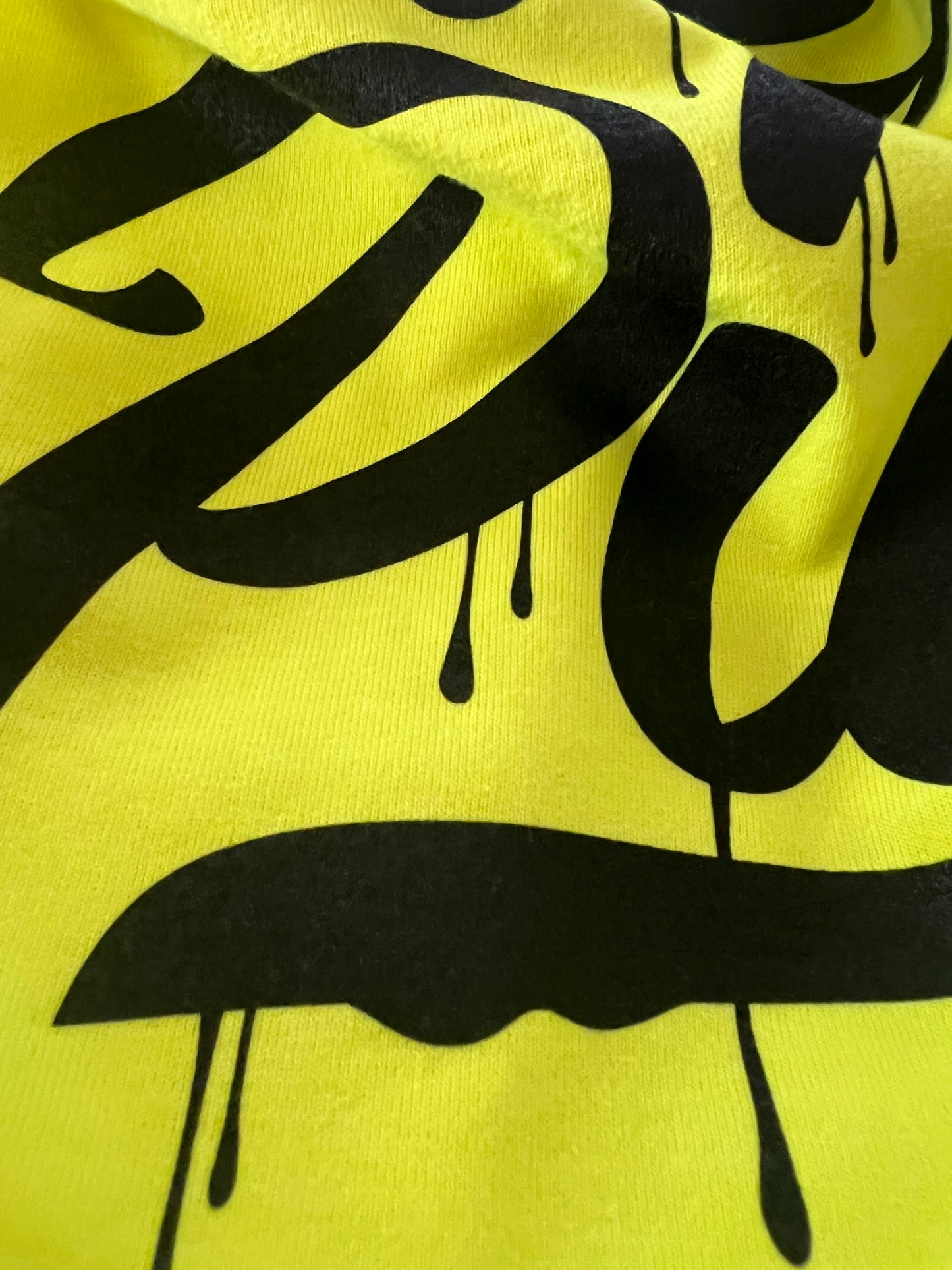 Detail shot of Pilas Clothing Co. PLP Drip Hi-Vis safety shirt in high-visibility yellow with bold black drip-style typography, displaying premium cotton fabric and screen print finish