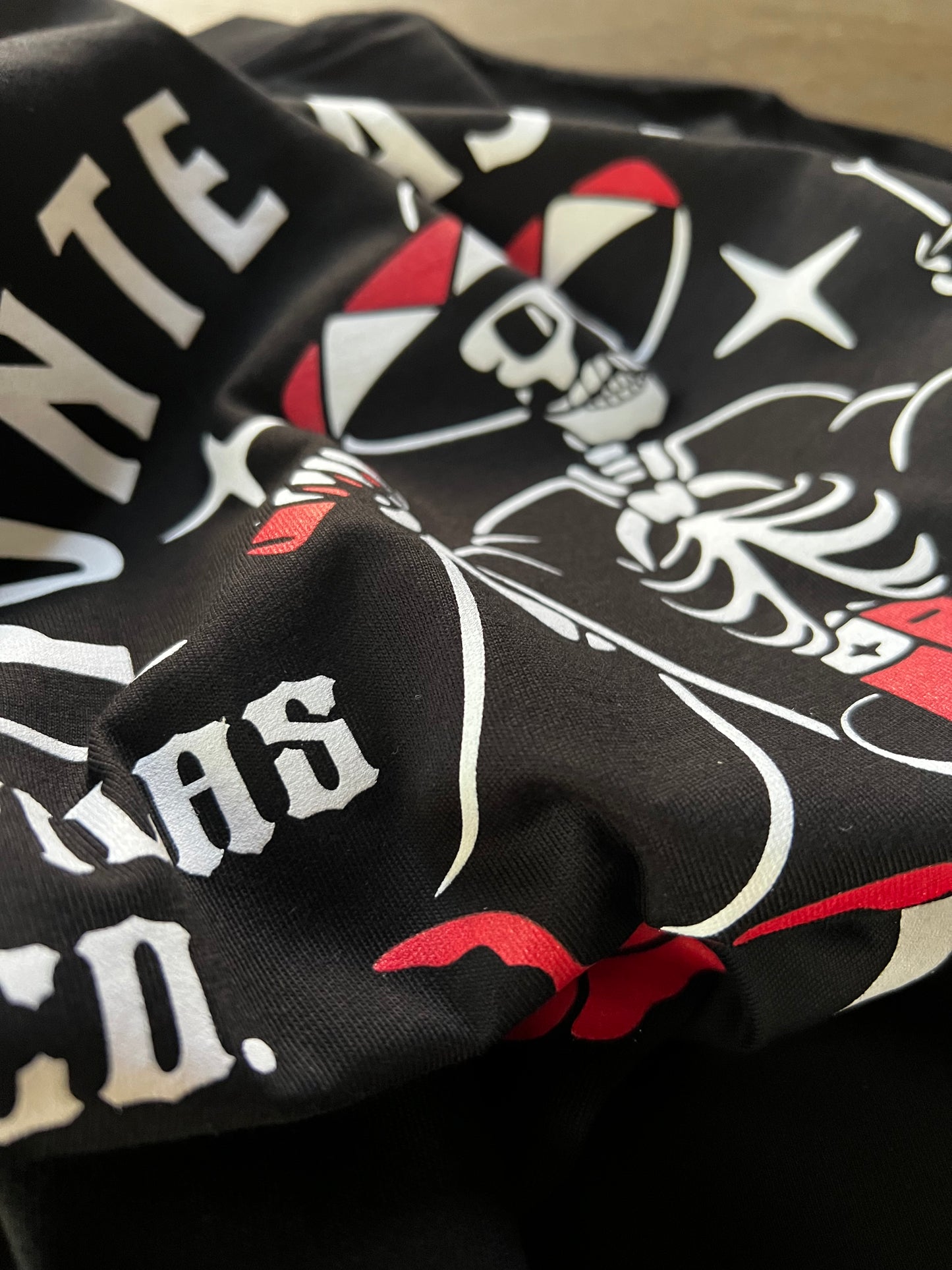 Close-up detail of Pilas Clothing Co. Mueve El Esqueleto dancing skeleton shirt in black with white, red and black tattoo-style artwork featuring skull, roses, and gothic lettering on premium cotton