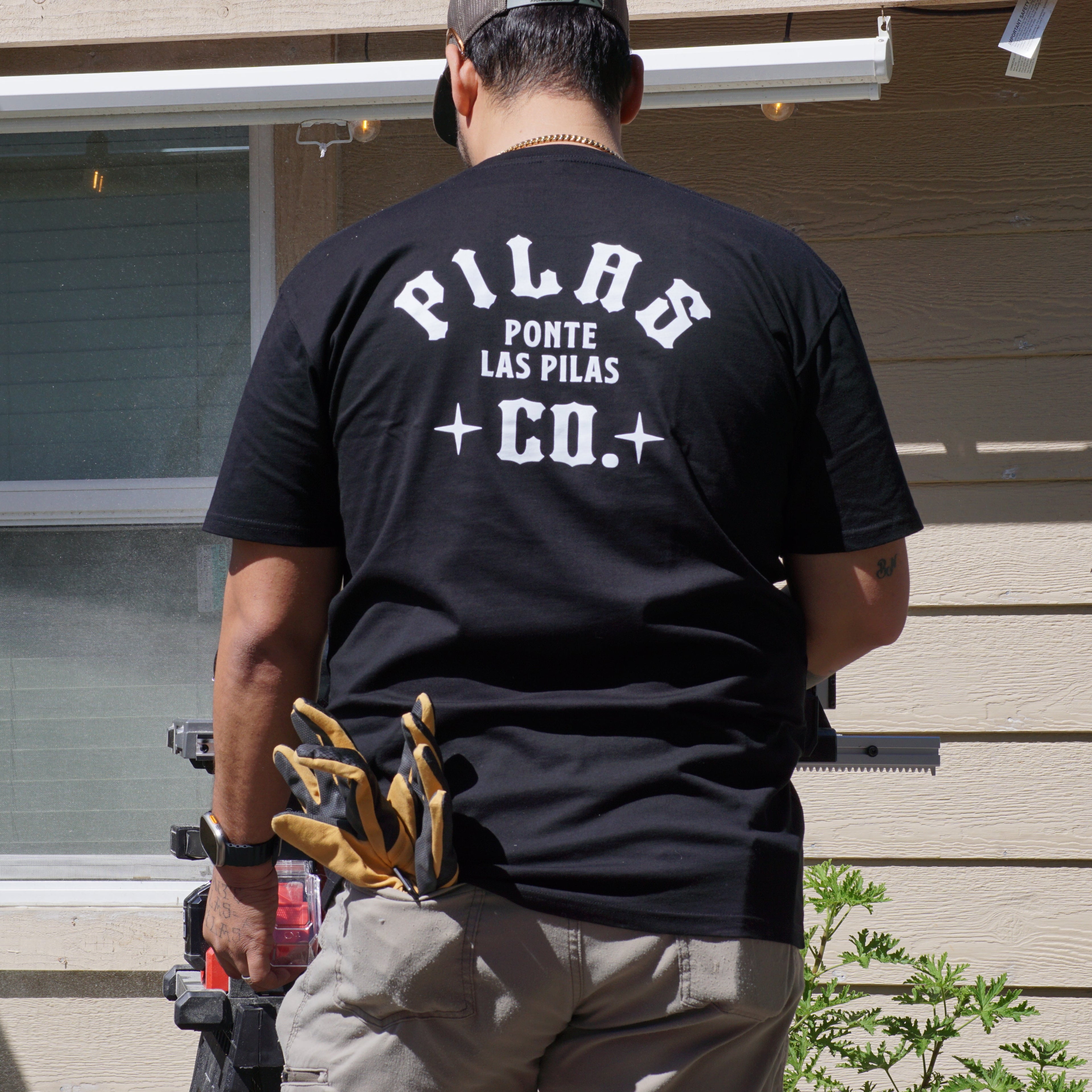 Latino construction worker wearing Pilas Co Ponte Las Pilas t-shirt back design with tool belt on job site