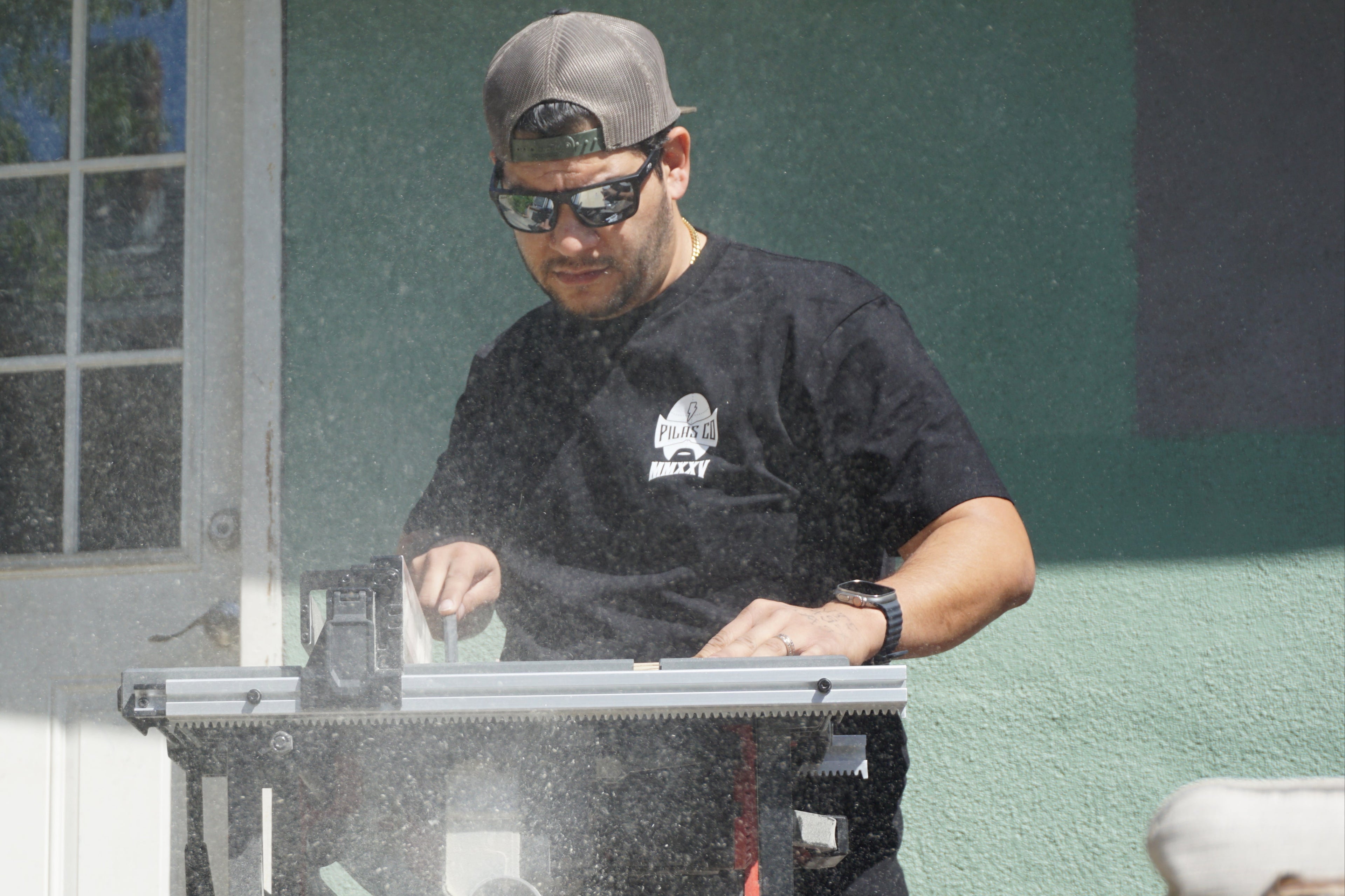 Latino construction worker wearing Pilas Co t-shirt using table saw - authentic workwear in action