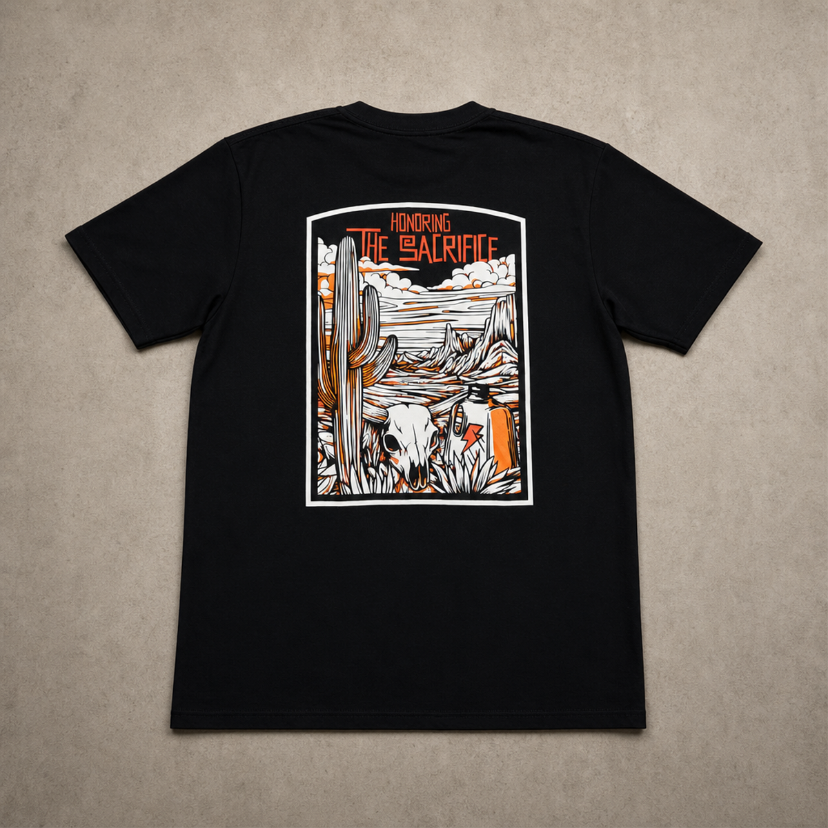 A black short-sleeve t-shirt laid flat on a textured beige background, showing the back side with a large rectangular graphic print. The graphic features desert scenery with saguaro cacti, a skull, and the text 'HONORING THE SACRIFICE' in orange.