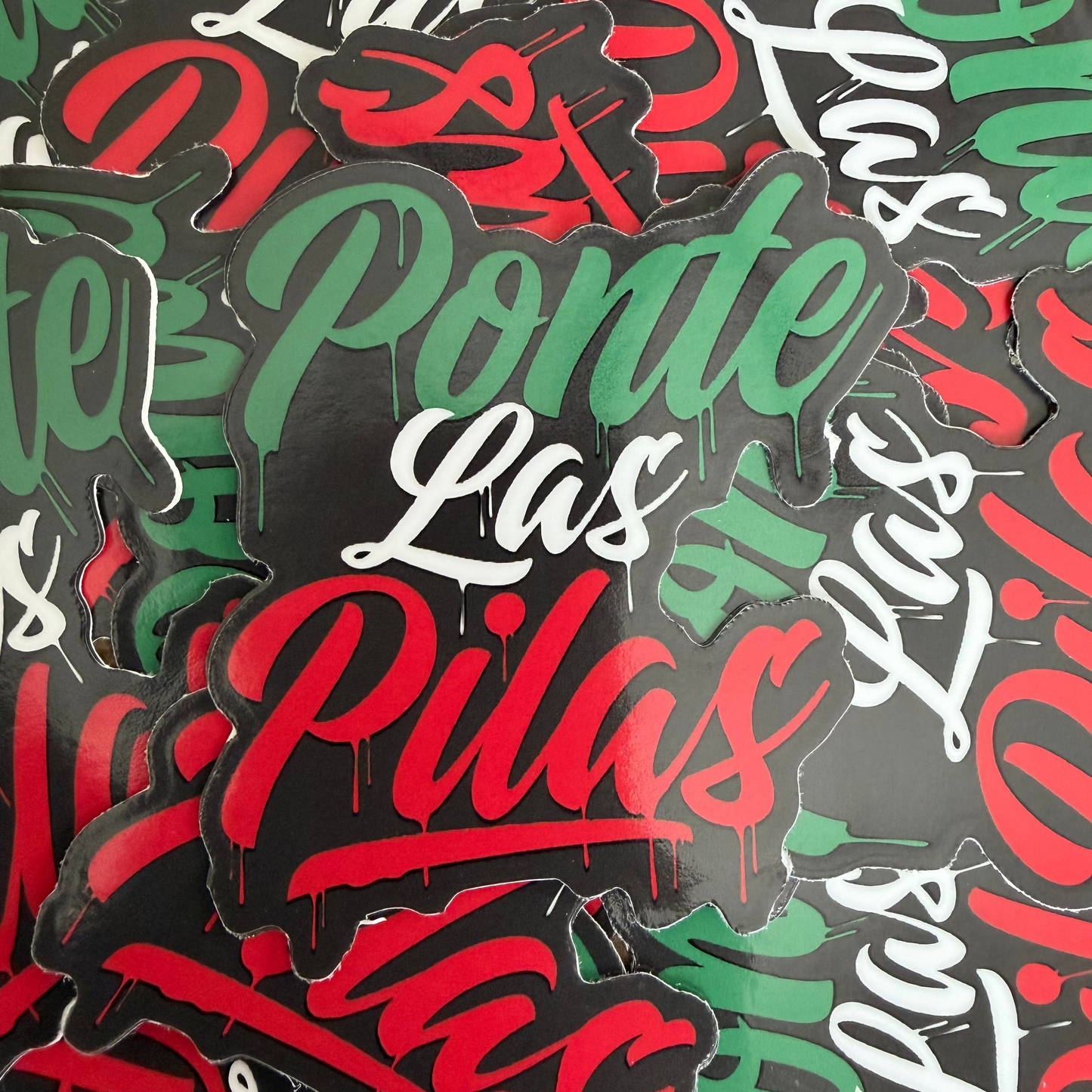 A pile of die-cut stickers featuring the phrase 'Ponte Las Pilas' in red, green, and white stylized lettering on a black background.