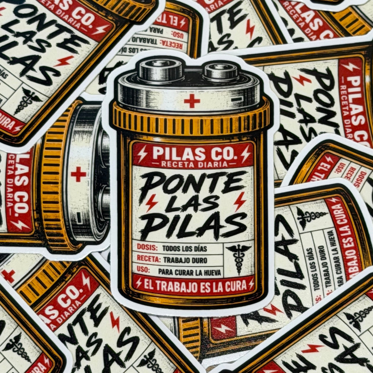A close-up flat lay of multiple die-cut stickers featuring a vintage-style battery can design with Spanish text reading 'PILAS CO. - PONTE LAS PILAS' and lightning bolt accents.