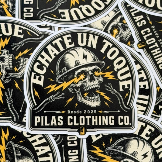 A close-up of multiple identical circular stickers or decals featuring a skull wearing a hard hat with lightning bolts, the text “ECHATE UN TOQUE,” “Desde 2025,” and “PILAS CLOTHING CO.” on a black background.