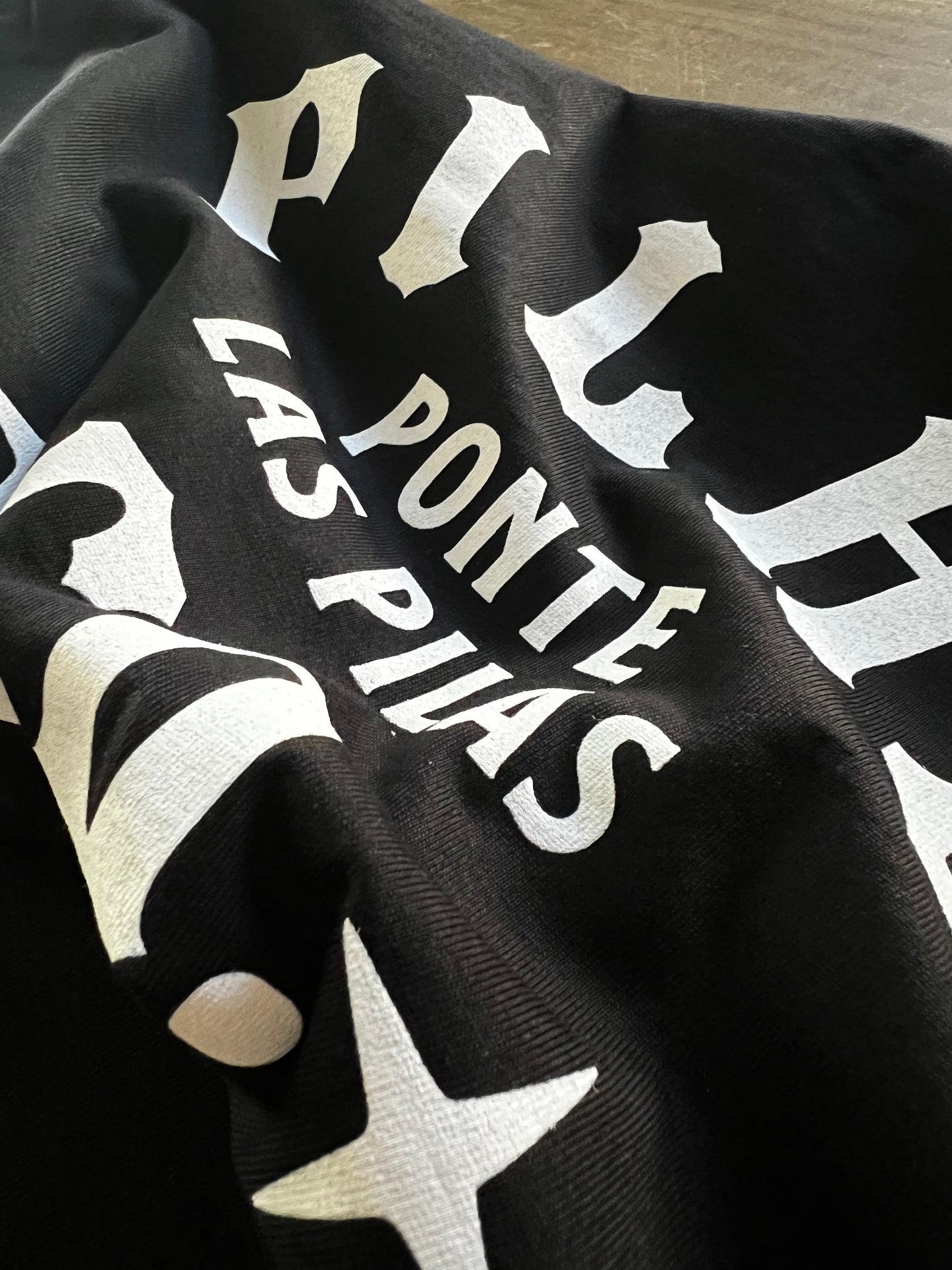 Detail shot of Pilas Clothing Co. PLP Ponte Las Pilas text shirt in black with white gothic-style typography, displaying heavyweight cotton material and bold contrast printing